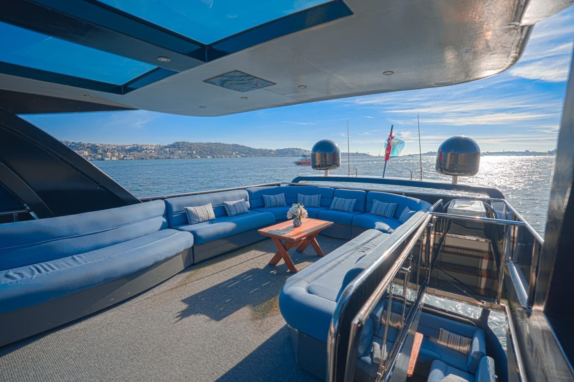 The open upper lounge of a Luma charter yacht in daylight, blue sofas and the Bosphorus beyond